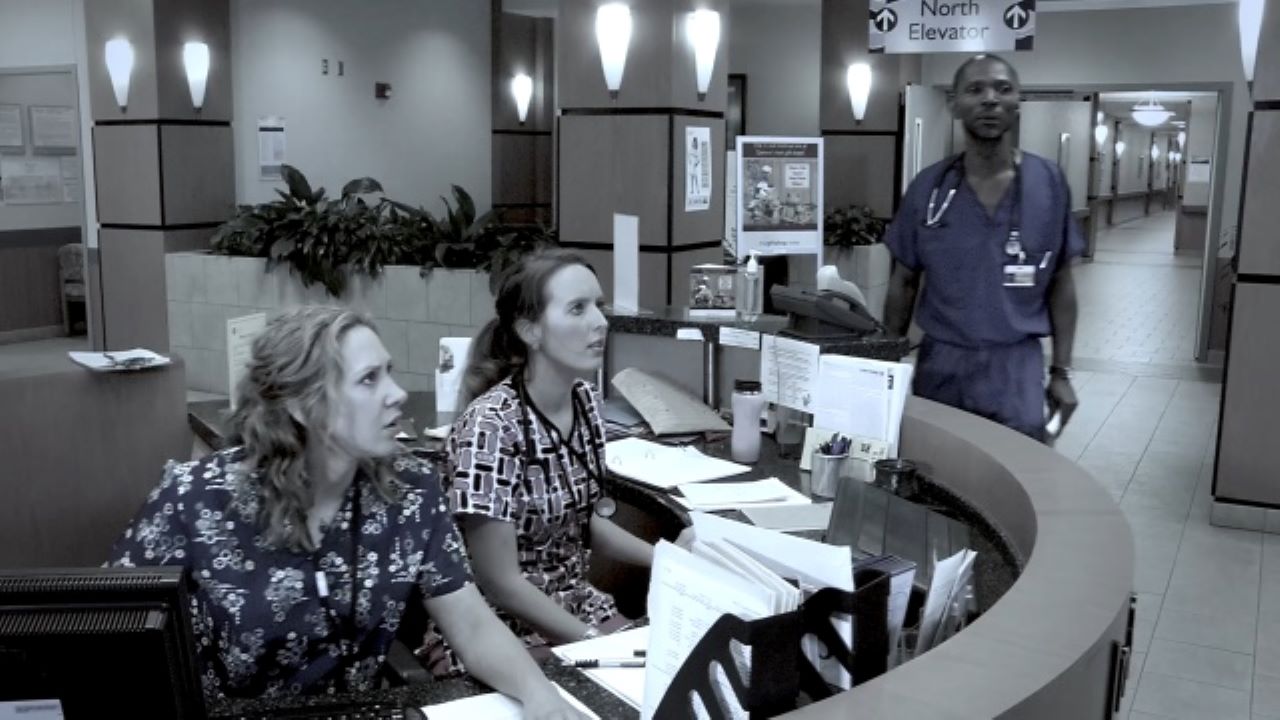 Healthcare workers seated at front desk look alarmed at something they're seeing