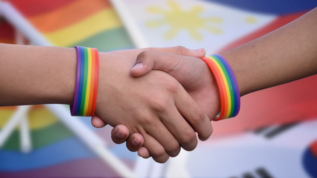two people shaking hands each wearing a rainbow wristband
